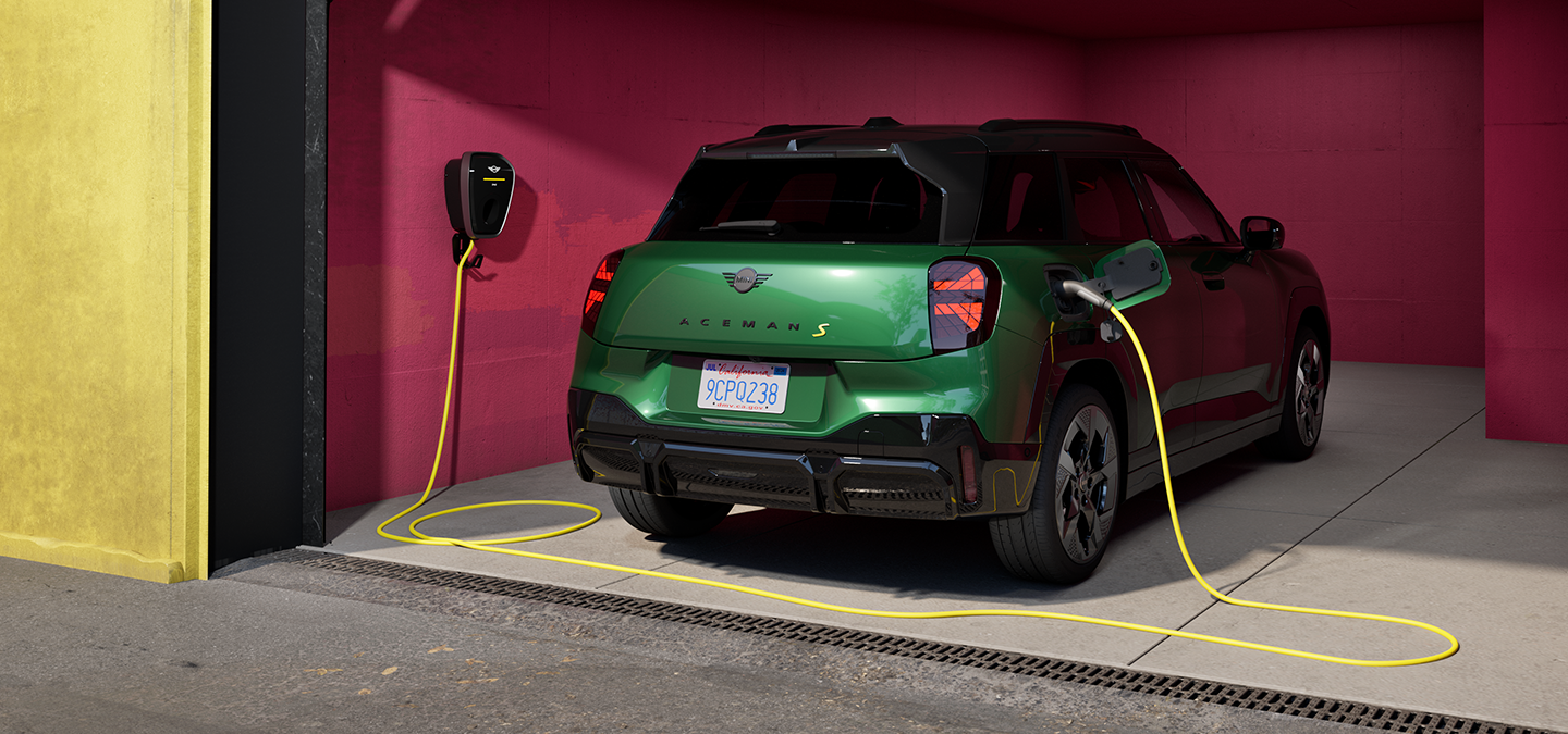 Rear view of the all-electric MINI Aceman in British Racing Green charging in a garage. 