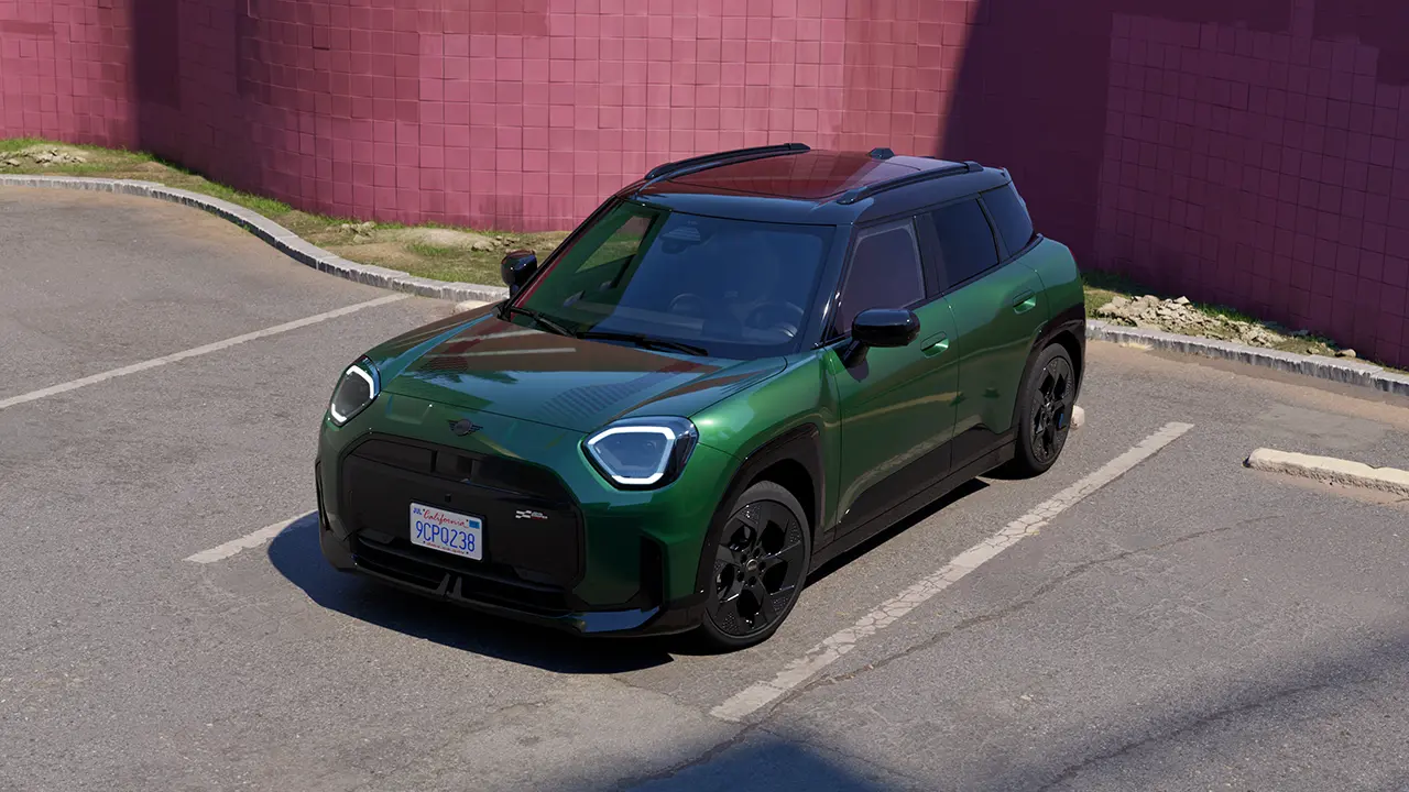 Frontal view of parking all-electric MINI Aceman in British Racing Green in parking lot with pink wall in the background