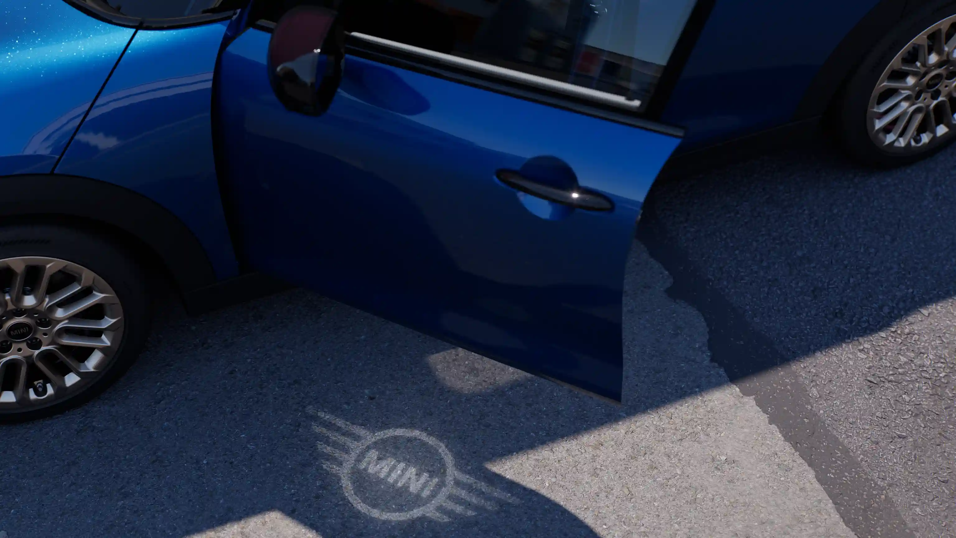 Exterior view of MINI Cooper 5-Door with open door and MINI logo welcome light on the ground 