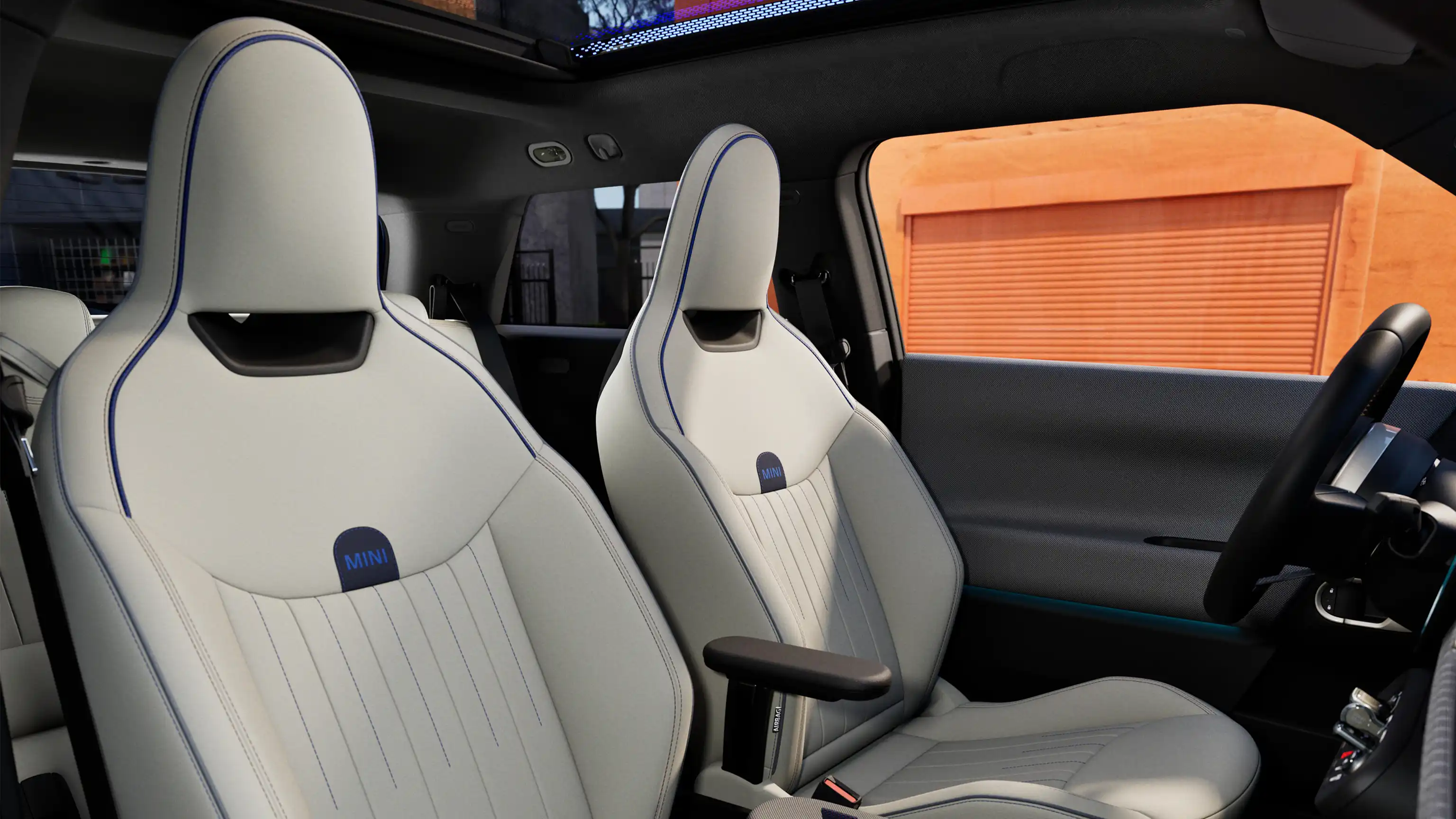 Interior perspective of the all-electric MINI Cooper is showing the dashboard, steering wheel, round display, panorama glassroof  and back of the frontseats