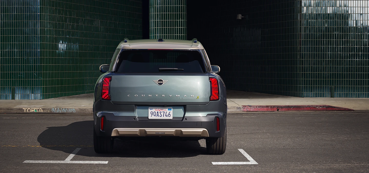 Rear view of the all-electric MINI Countryman in Smokey Green and Vibrant Silver roof parking. 
