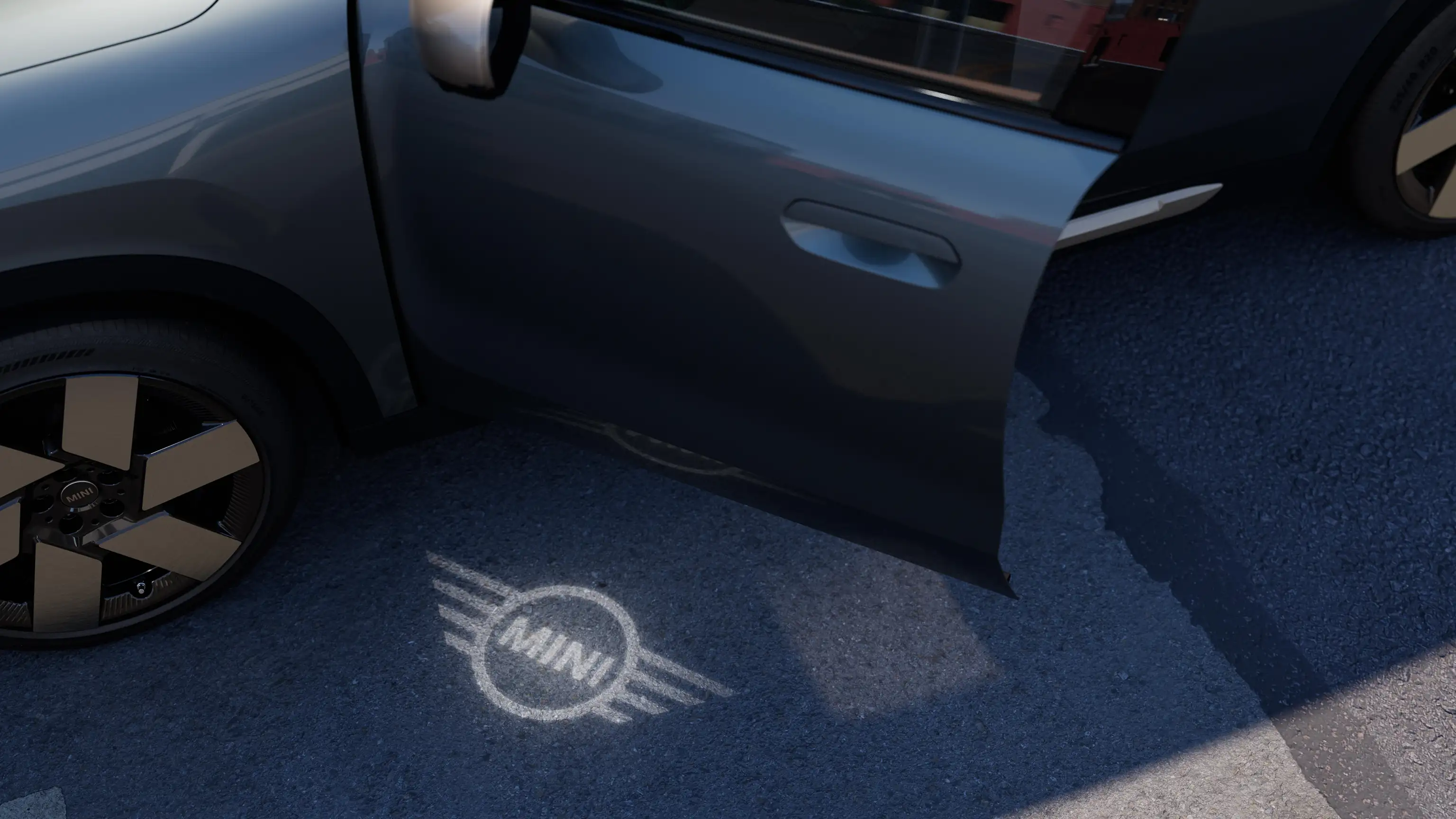 Exterior view of all-electric MINI Countryman with open door and MINI logo welcome light on the ground 