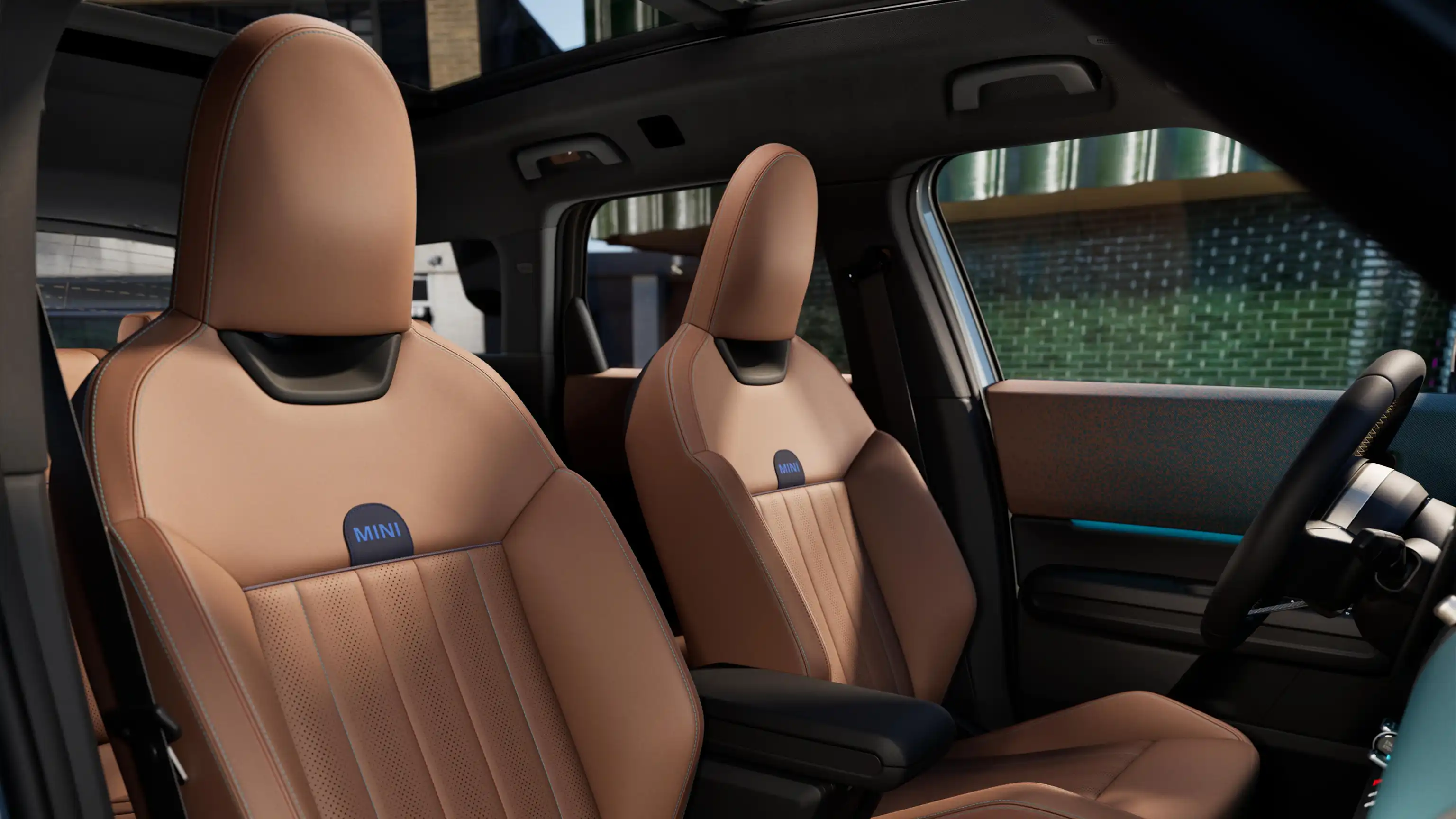 Interior perspective of the all-electric MINI Countryman is showing the dashboard, steering wheel, round display, panorama glassroof and back of the frontseats.