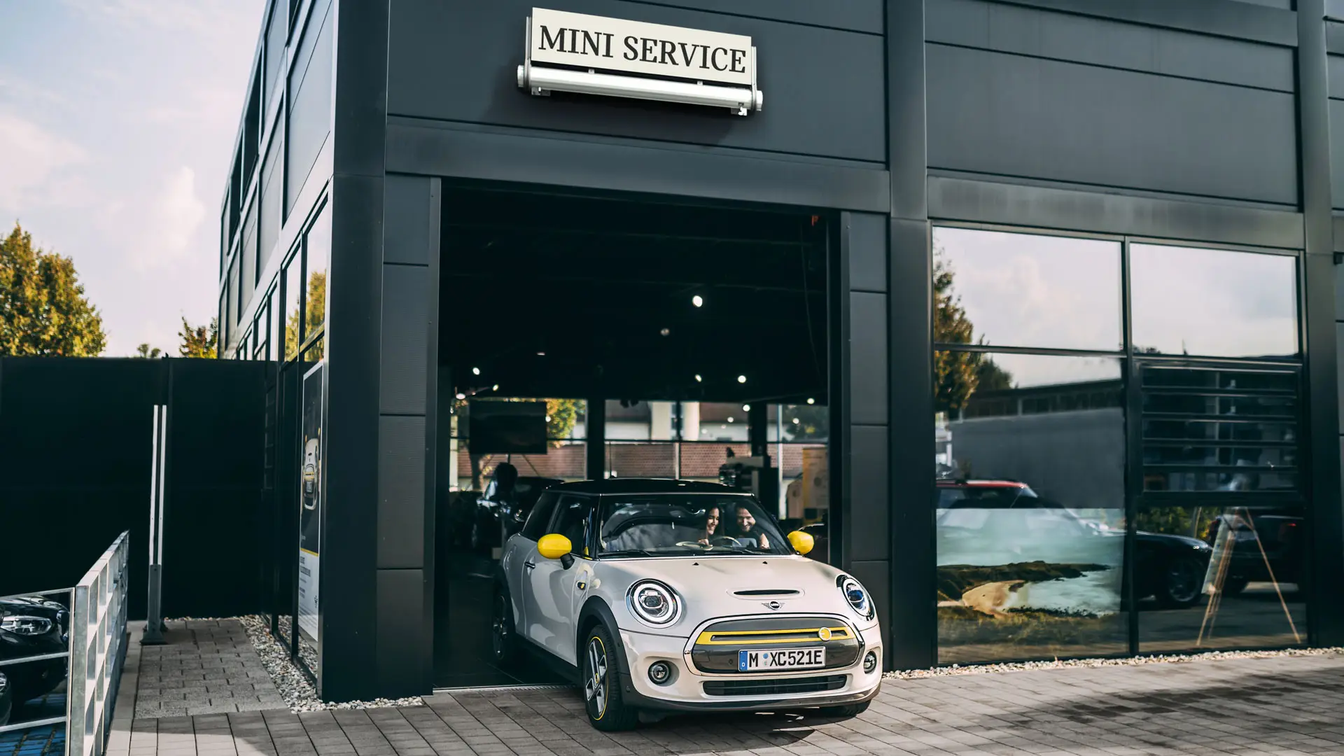お客様が、新車のMINIエレクトリックを運転し、MINIサービス・パートナーの店舗前へと進んでいきます。