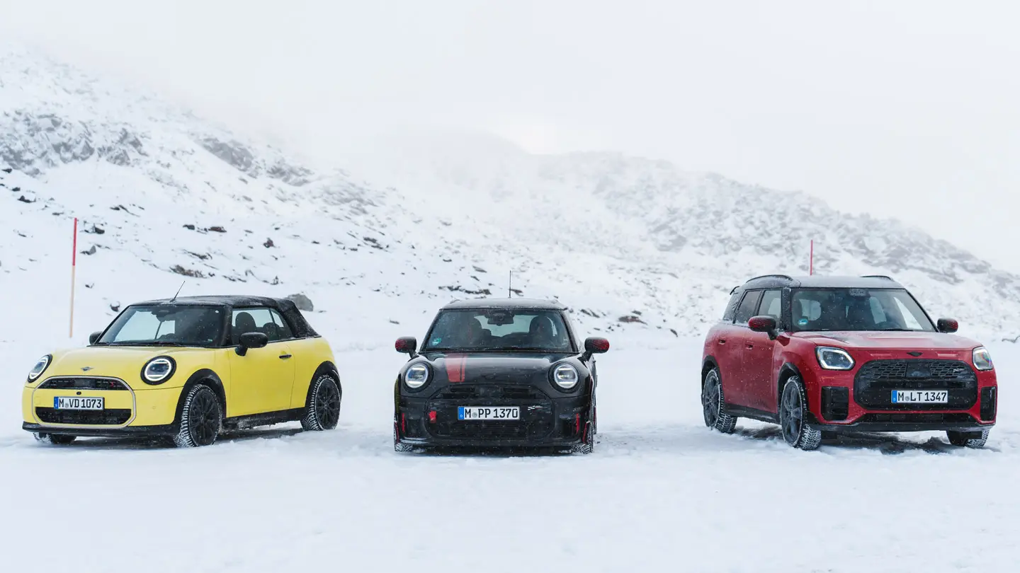 雪に覆われた山道に停車している3台のMINI（正面からの眺め）。
車種とカラーは、MINI Cooper Convertible（サニーサイド・イエロー）、MINI John Cooper Works（ミッドナイト・ブラック II）、MINI Countryman Cooper（チリ・レッド）です。
