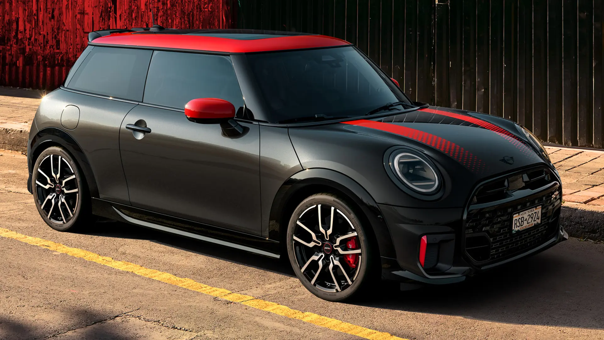 MINI John Cooper Works 3ドアミッドナイトブラック、ルーフキャップとミラーキャップはチリレッド、スポーツストライプレッドはレッドで、サイドビュー、路上駐車時。