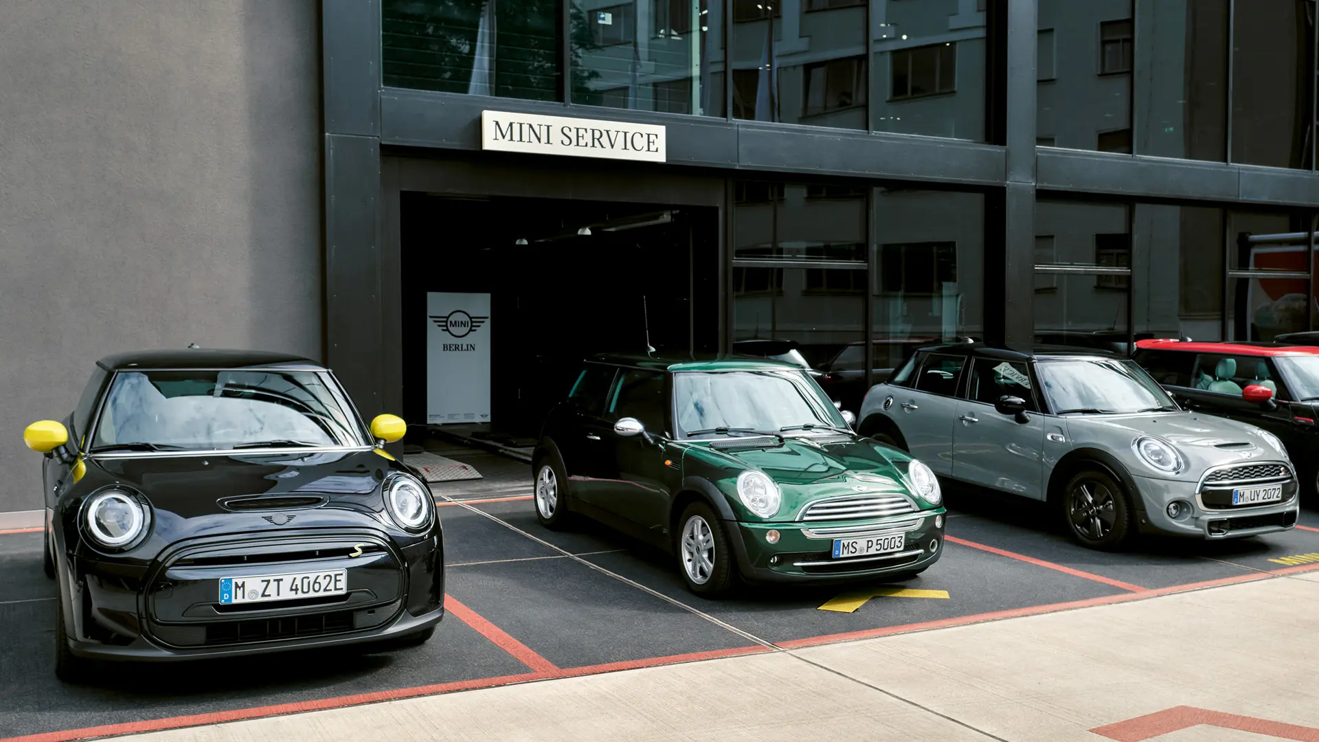 MINI Cooper Electric S（黒）がMINI Center の外に立っている。MINI Cooper Electric S（グリーン）、MINI 5ドア（シルバー）、MINI JCW（黒）の正面図。 