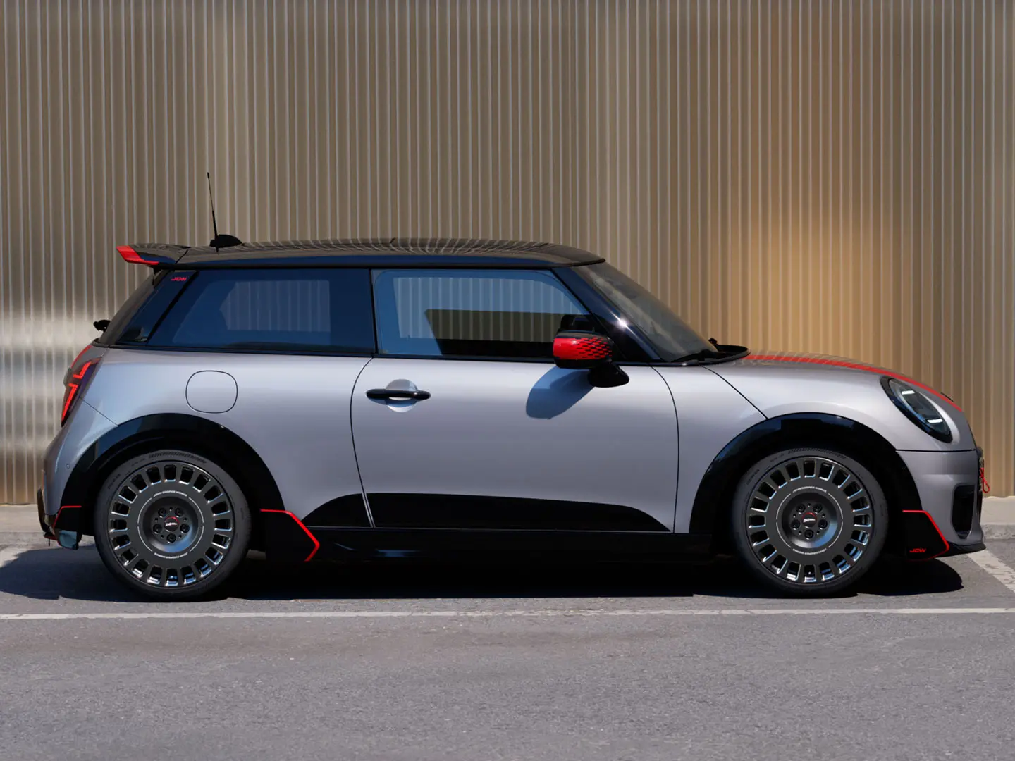 メルティングシルバーのMINI Cooper 3ドアを横から捉えた画像です。空力性能を高めるためのジョン・クーパー・ワークス製ルーフスポイラーが特徴です。